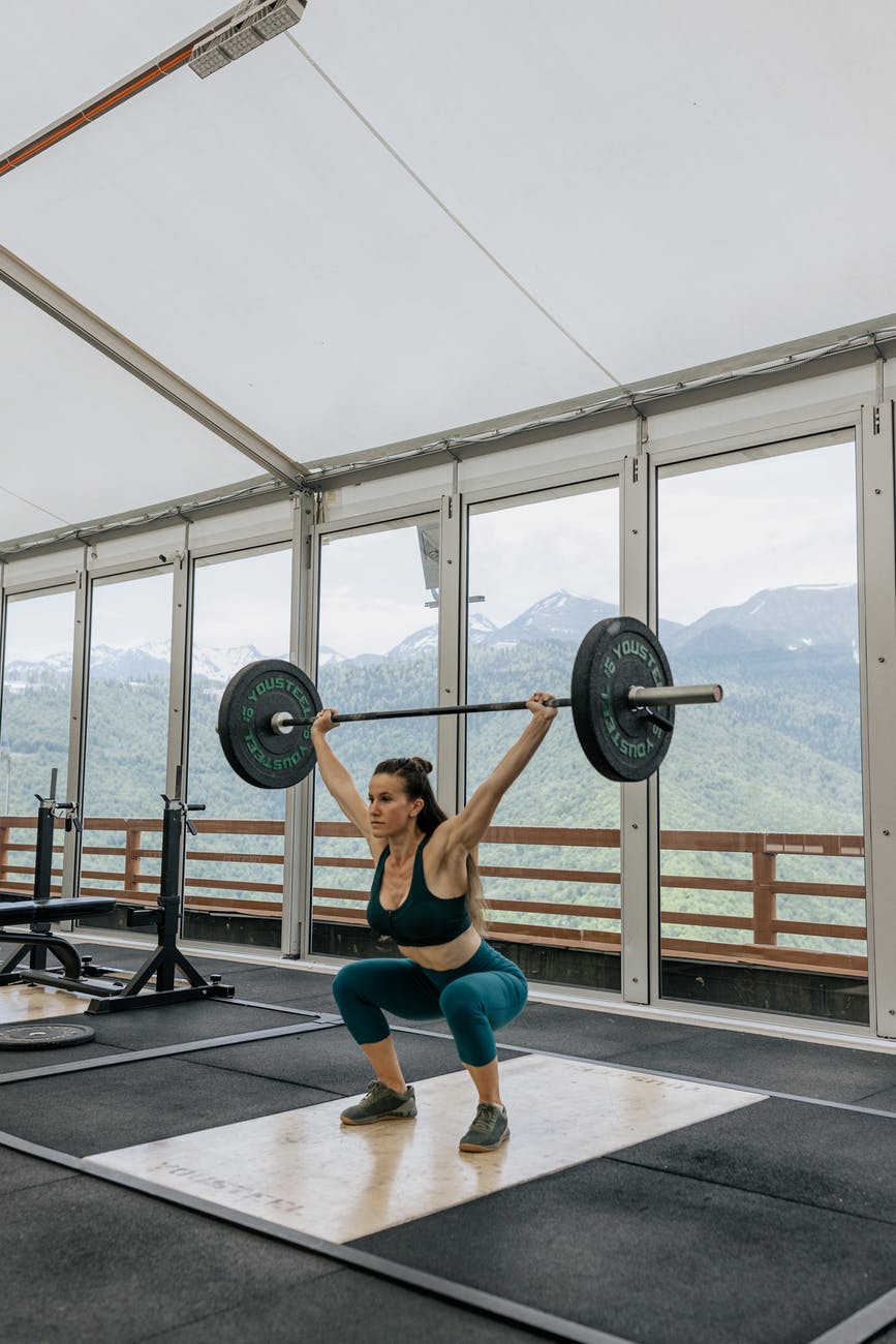 woman holding black barbell beside windows